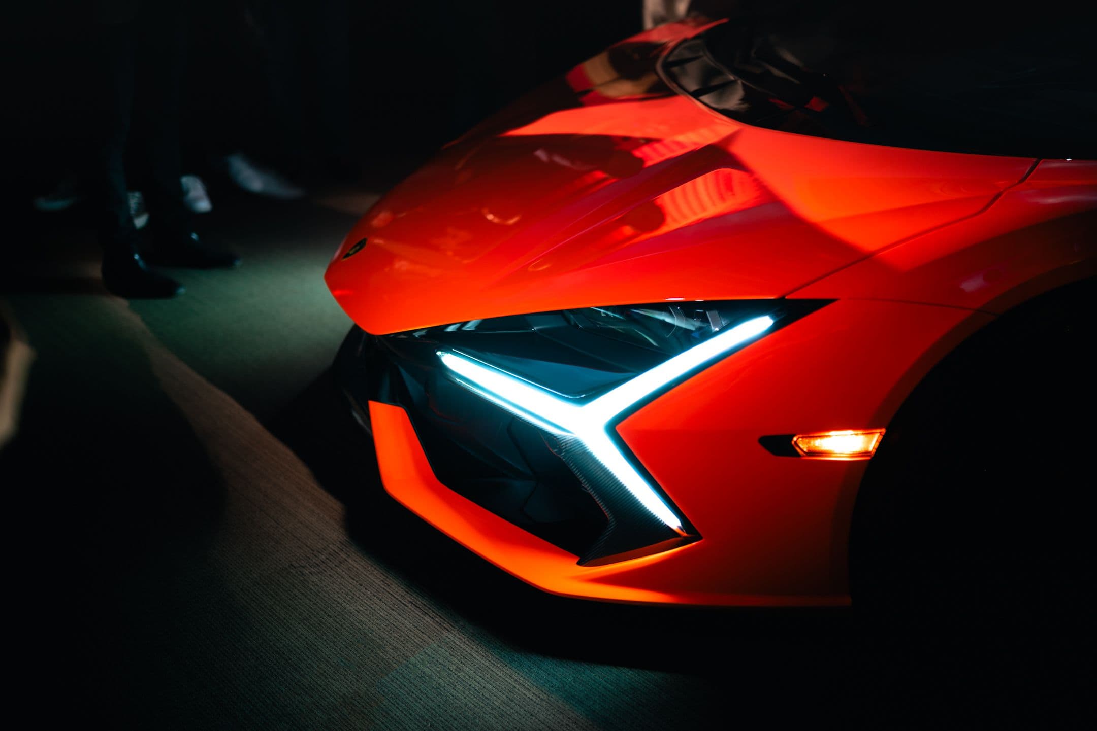 Close-up of Lamborghini Revuelto front LED headlights with Y-shaped DRL signature in low-light showroom setting.
