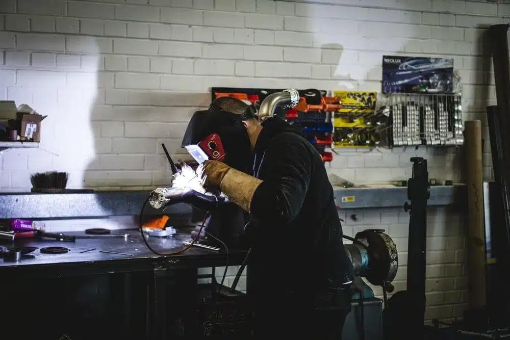 Fabricator at JBM Performance welding a custom automotive part in a performance shop.