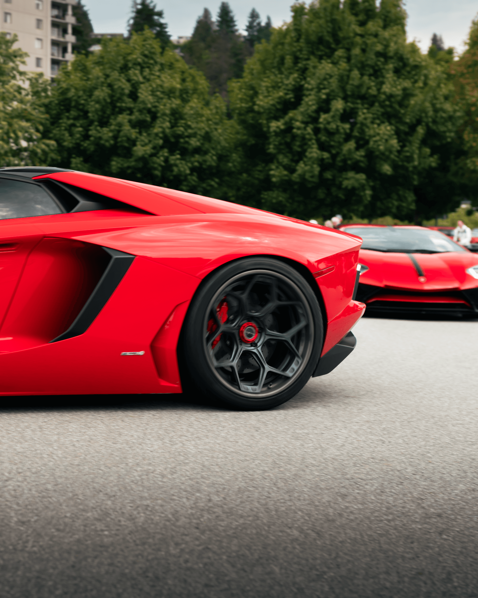Rear quarter view of a red Lamborghini Aventador SVJ with exposed carbon fibre accents and centre-lock wheels, parked in front of a red LaFerrari at a supercar meet.
