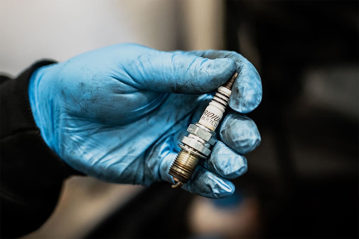 A technician holding a used spark plug during an engine inspection to diagnose detonation or pre-ignition issues.