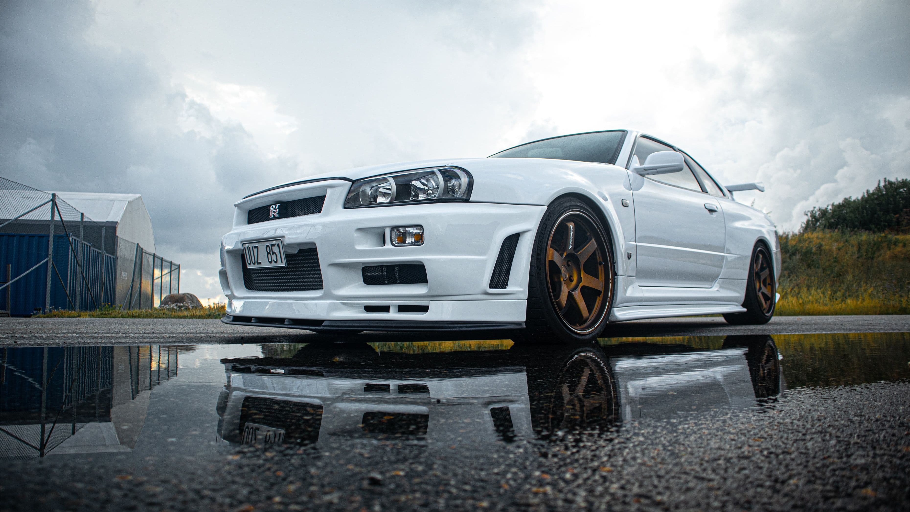 White Nissan Skyline GT-R R34 reflected in a puddle on an overcast day.