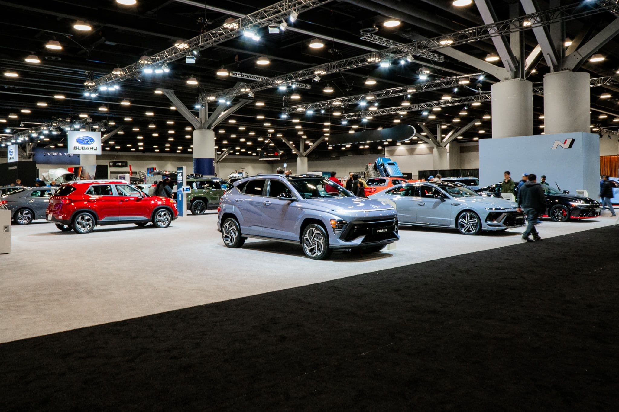Hyundai display at the 2025 Vancouver International Auto Show, featuring a lineup of new models under bright exhibition lighting. Multiple other manufacturers, including Subaru, are visible in the background, showcasing a wide variety of vehicles to attendees exploring the event.