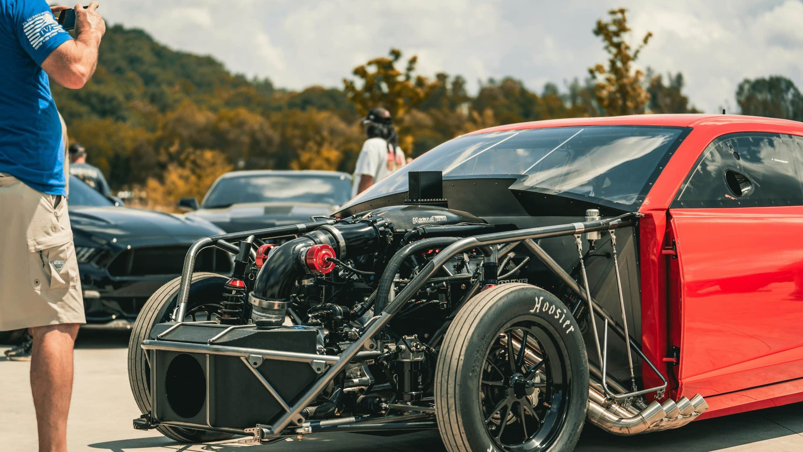 Red drag racing car with exposed twin-turbo engine setup on display at a car event.