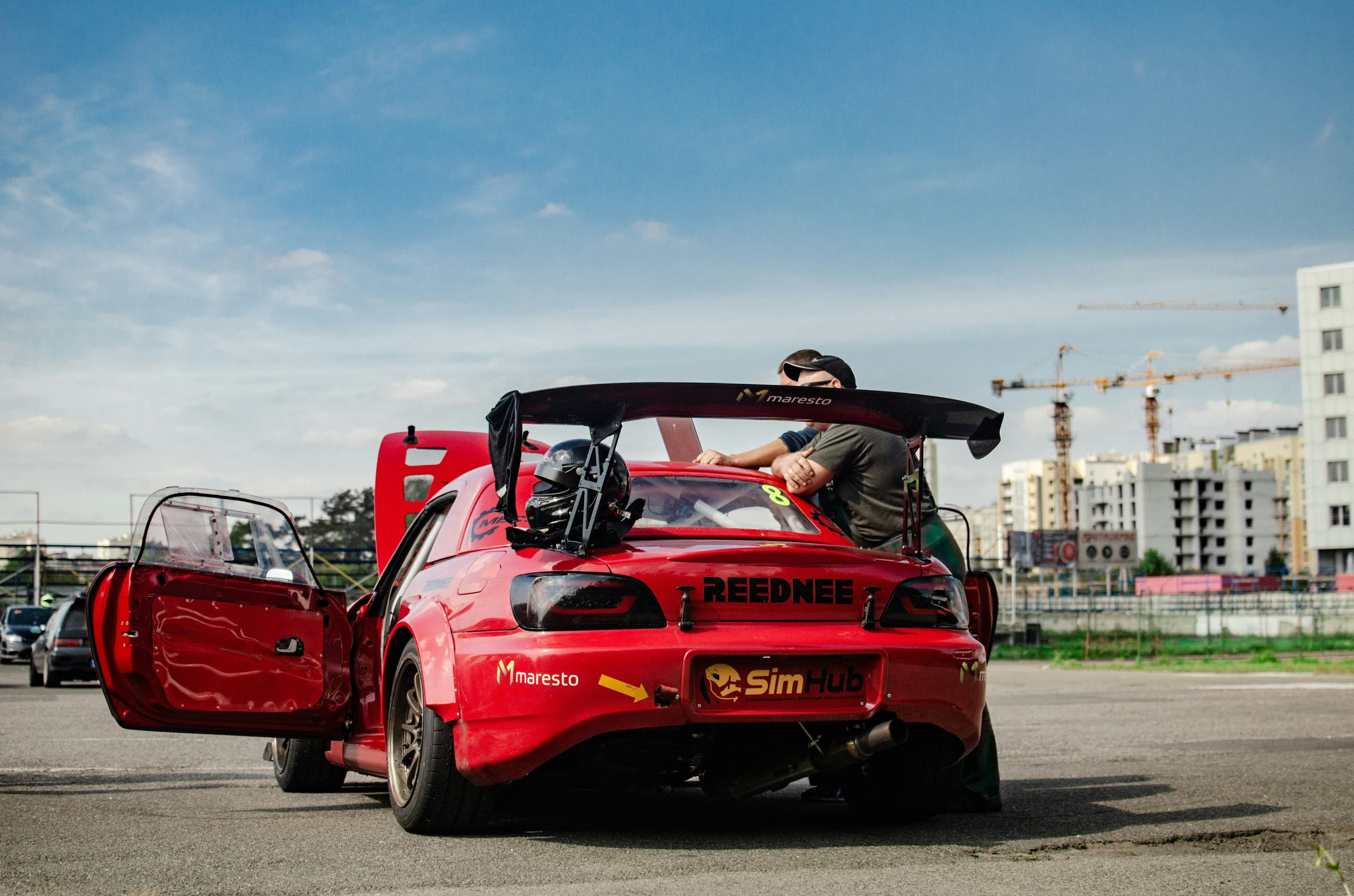 Red Honda S2000 with a large rear wing and track modifications at a racing event. Track-ready setup with helmet and racing decals.