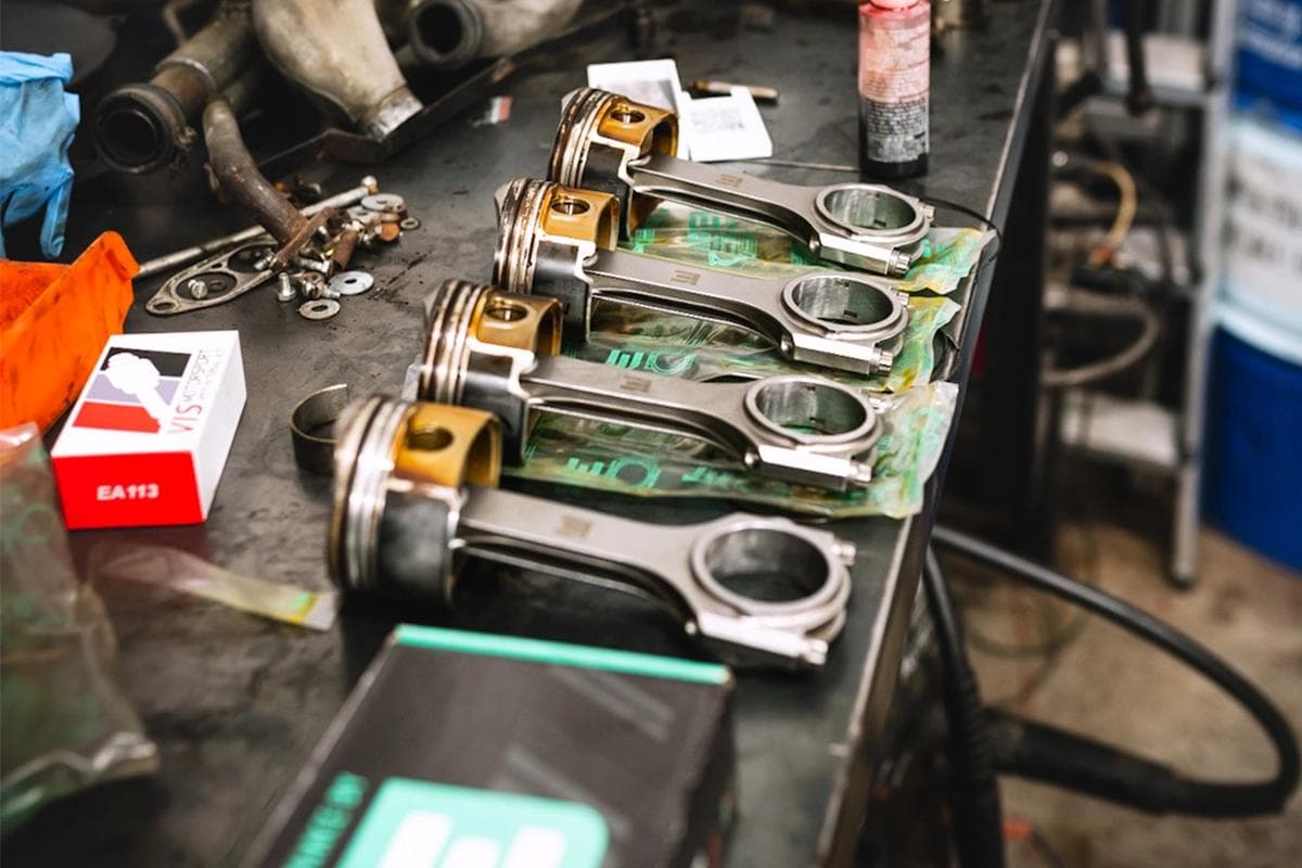 EA113 2.0 TFSI AXX pistons fitted with Integrated Engineering connecting rods laid out on a workshop bench during engine build preparation.