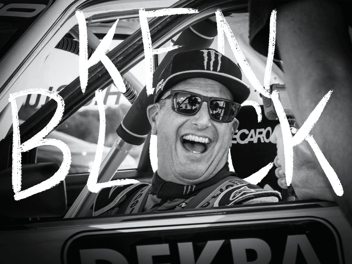 Ken Block smiling while seated inside an Audi race car, wearing sunglasses and a Monster Energy cap. The handwritten text 'Ken Block' is displayed prominently over the image.