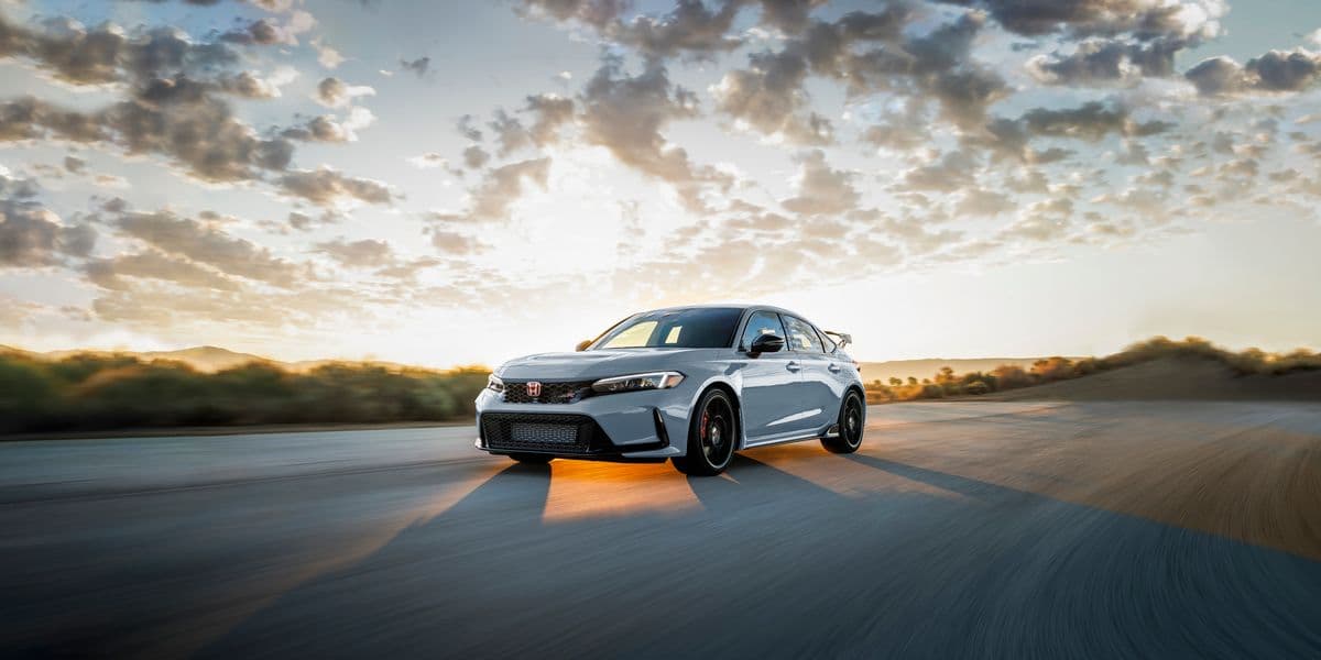A 2023 Honda Civic Type R in white driving at speed on an open road during sunset, with dramatic lighting and motion blur emphasising its aggressive stance and performance-focused design.