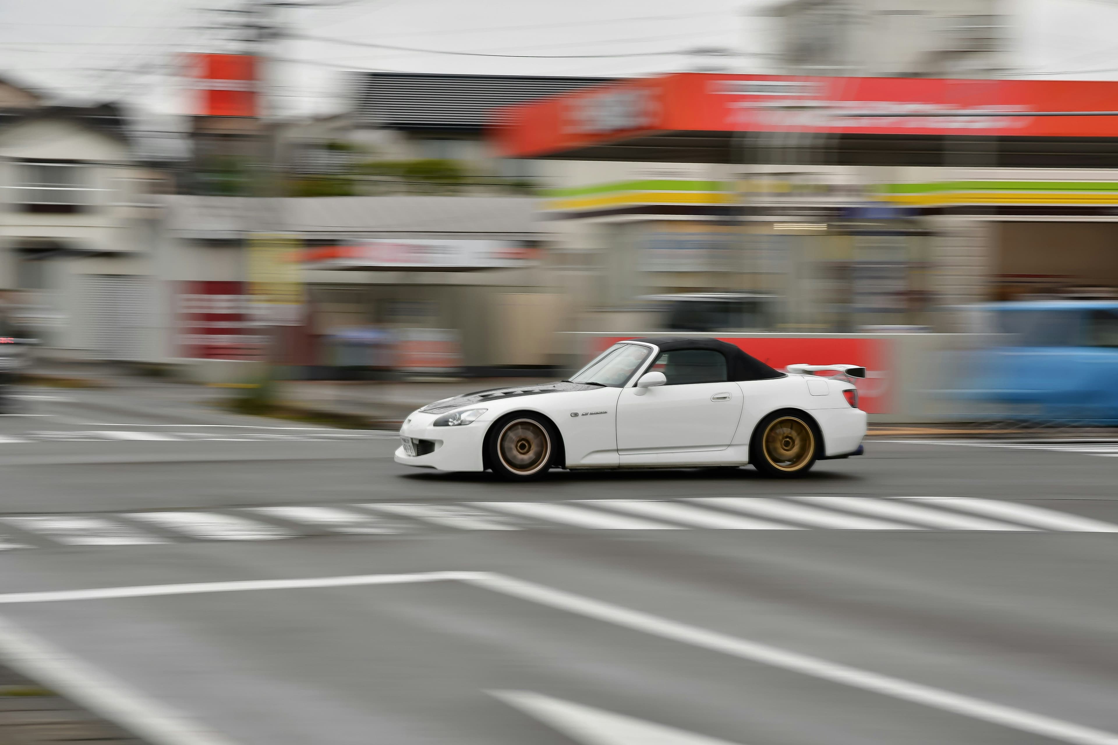 White Honda S2000 in motion on urban streets. Captured with a motion blur effect, emphasizing its performance-oriented design.