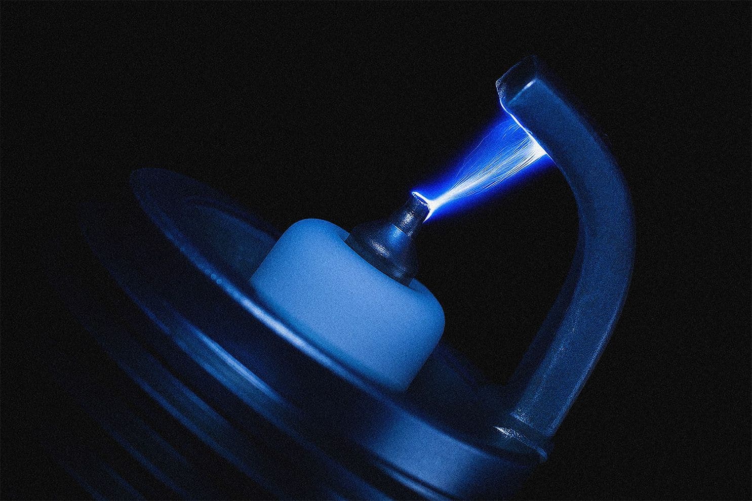 Close-up of a spark plug firing a vivid blue ignition arc, highlighting the precise moment of combustion initiation in an internal combustion engine.